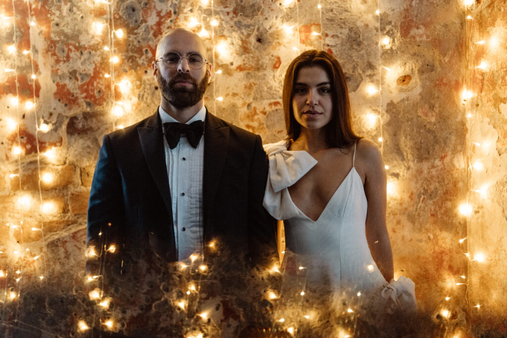 Married couple standing in front of pretty wall lights.